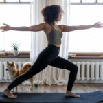 A woman doing yoga on a mat with her dog in a cozy home setting.